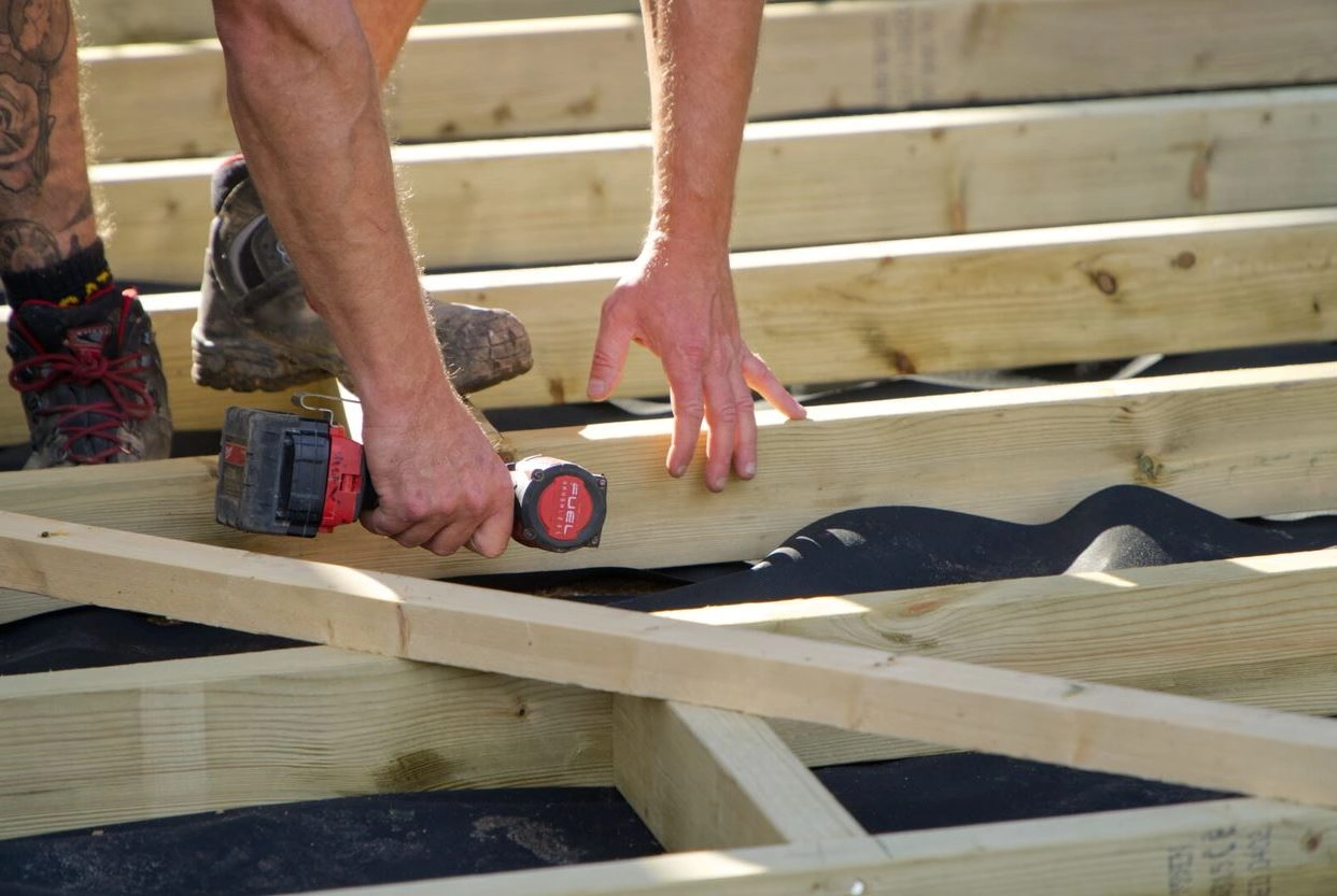 A person using decking joists to fit a deck using a screw driver.