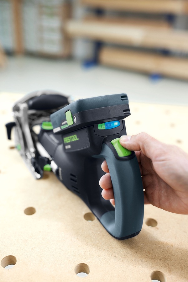 Nahaufnahme der Festool Akku-Dübelfräse DFC 500 in Aktion. Eine Hand betätigt den ergonomischen Griff, während die LED-Akkuanzeige den aktuellen Ladezustand deutlich sichtbar macht. Die Fräse liegt dabei auf einer Werkbank.