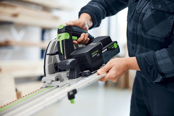 Nahaufnahme einer Person, die die Festool HKC 55 K Akku-Handkreissäge zusammen mit einer Führungsschiene hält. Das Bild zeigt die Handhabung des Geräts in einer hellen, professionellen Werkstattumgebung.