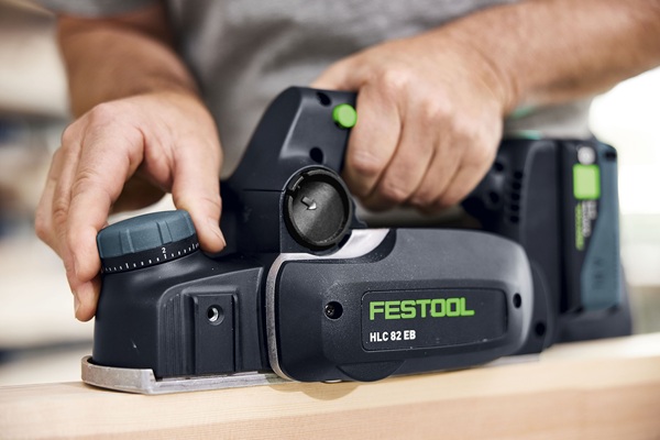 Nahaufnahme eines Handwerkers, der präzise mit dem Akku-Hobel Festool HLC 82 EB ein Holzstück bearbeitet. Dabei sind die ergonomische Handhabung und die genaue Einstellbarkeit gut erkennbar.