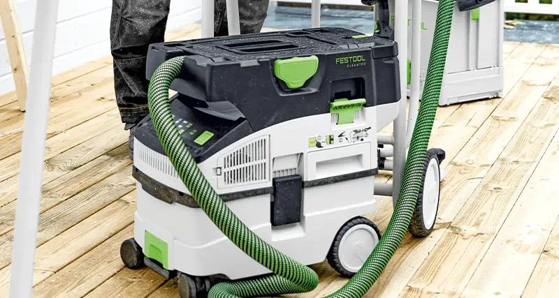 Festool Absaugmobil mit grünem Saugschlauch auf einer Holzterrasse im Einsatz.