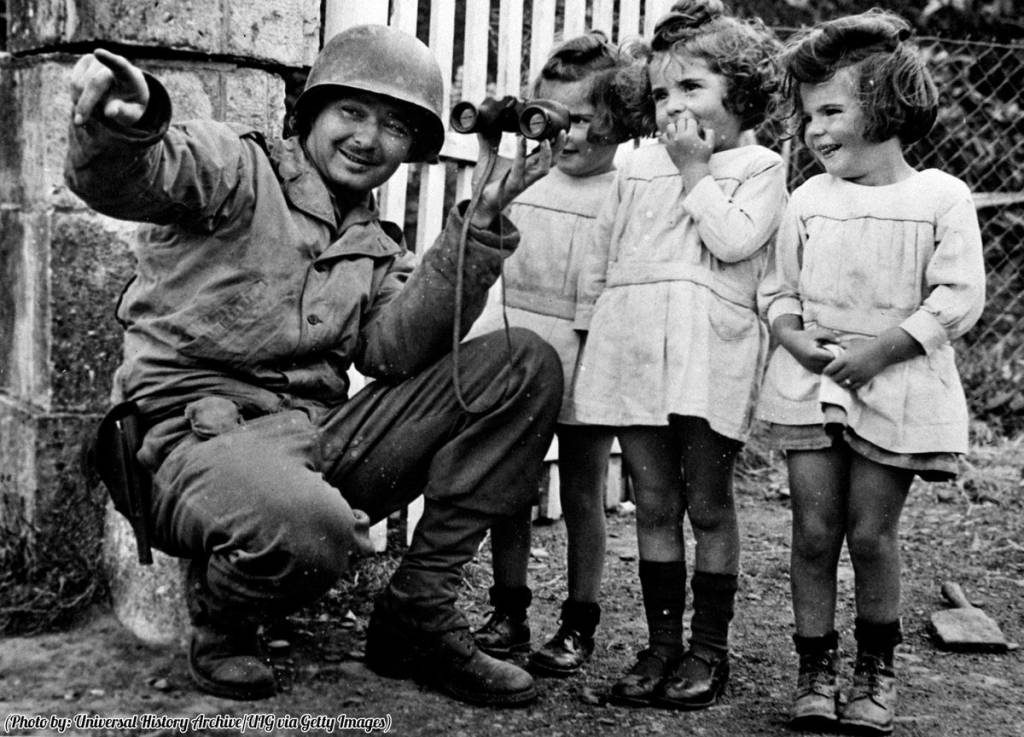 soldier shares his binoculars with three girls after the liberation of Normandy