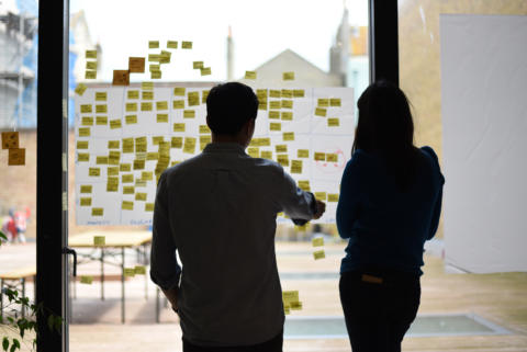 Two people having a discussion in front of a wall of post-it notes.
