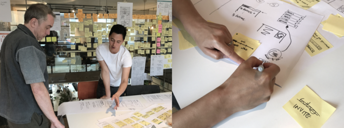 Two people having a discussion in front of a wall covered in post-it notes.