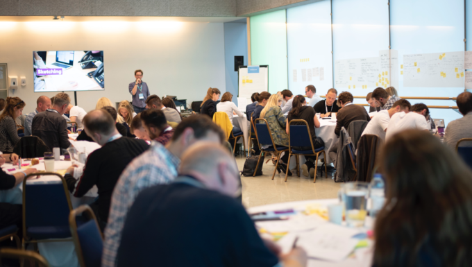 Chris running a design sprint workshop in a large glass room at UX London