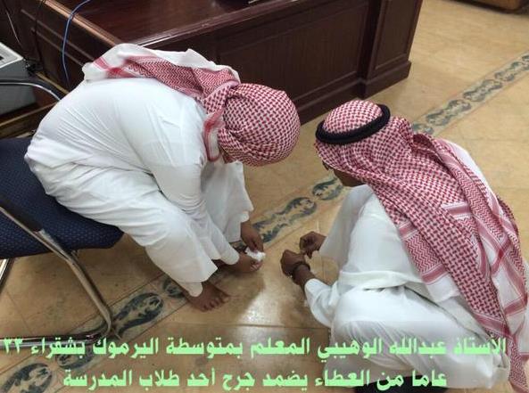 معلم على الأرض مُجلساً أحد طلابه على الكرسي لتضميد جرح بقدمه