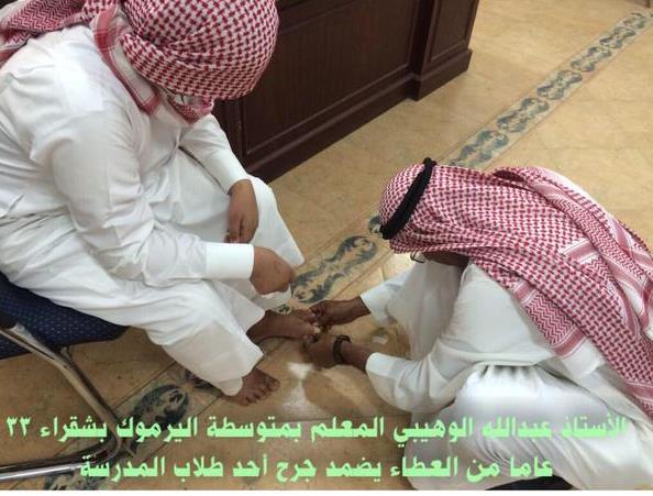 معلم على الأرض مُجلساً أحد طلابه على الكرسي لتضميد جرح بقدمه