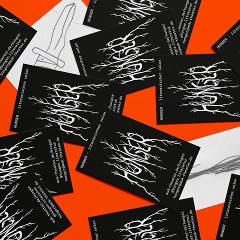 Scattered black and white business cards on an orange surface featuring a white abstract root-like design and text including 'HUNGER literarischer salon' and a website URL