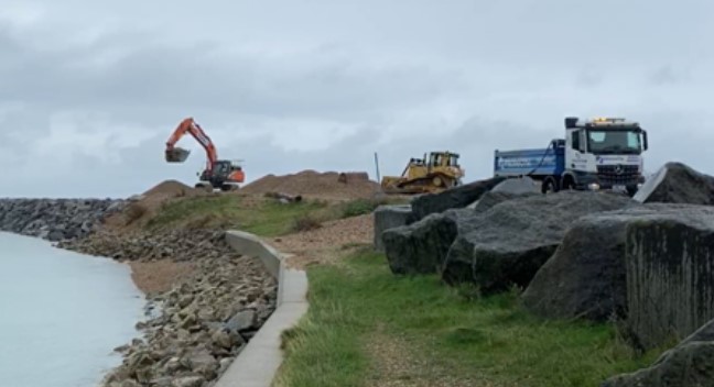 Excavator, bulldozer and lorry working on a shingle beach as part of the bypassing process.