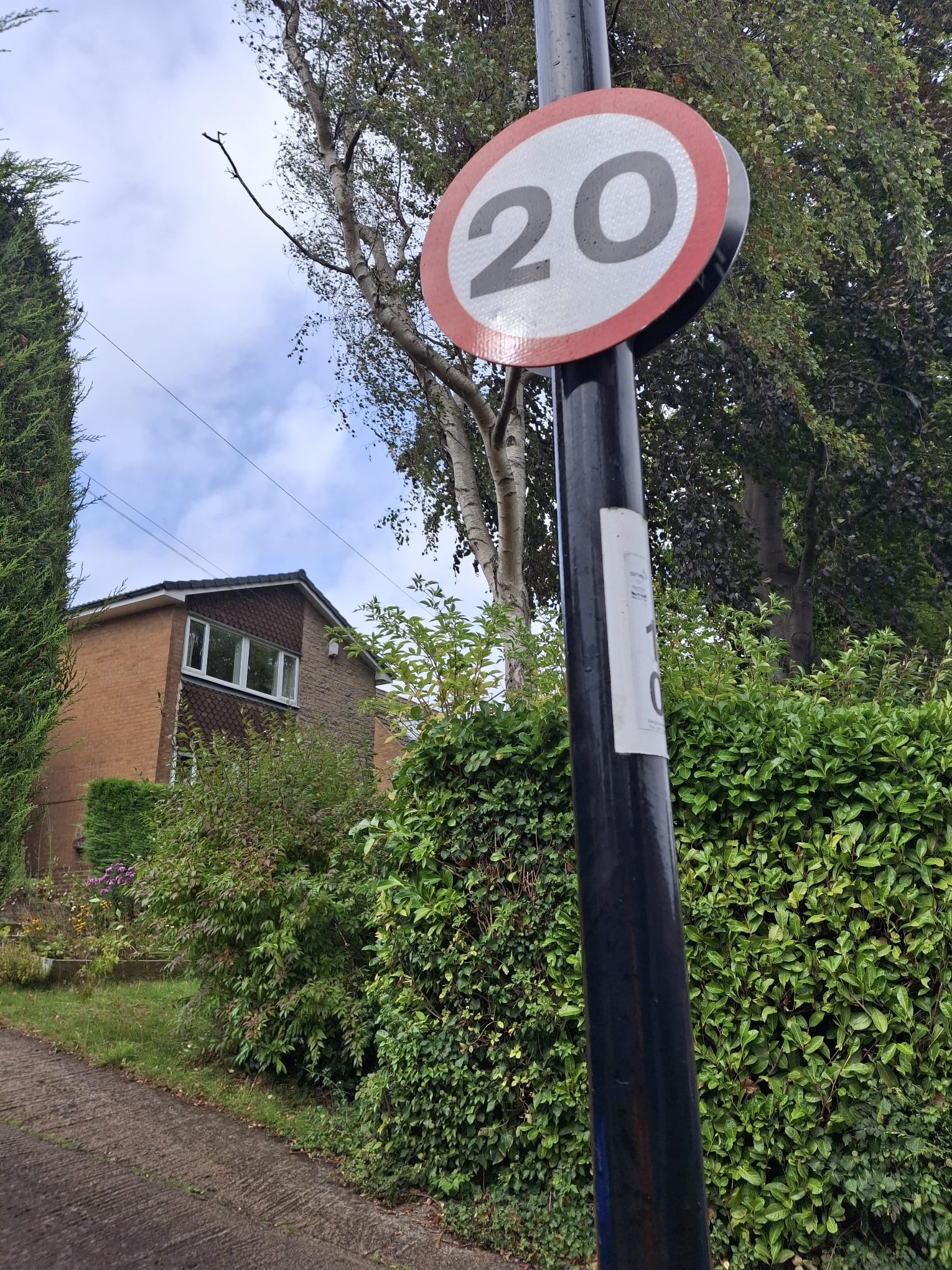 A road sign displaying a 20mph speed limit in front of a residential property 