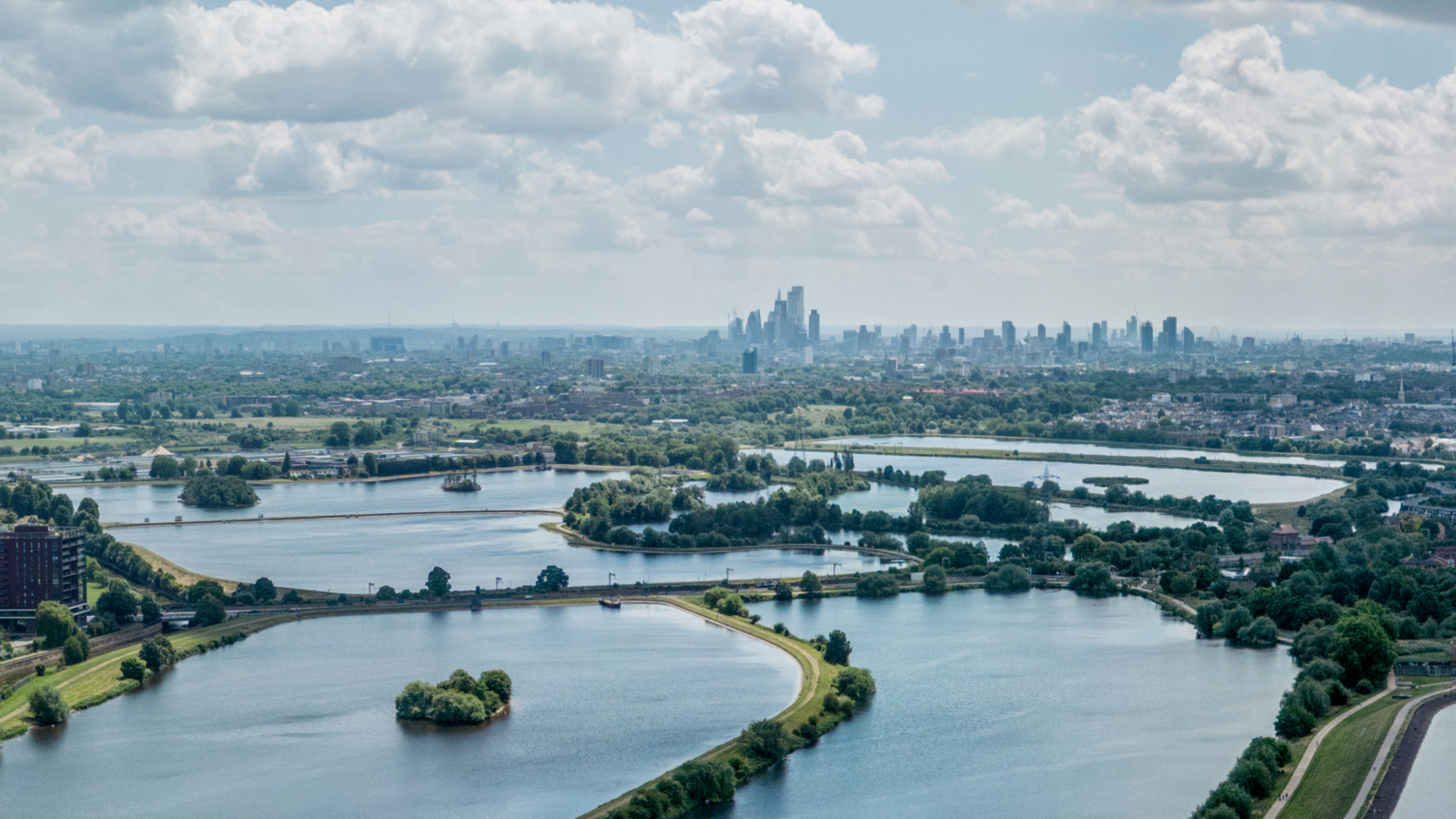 Aerial view of a scenic landscape with winding waterways and islands, leading to a distant city skyline under a partly cloudy sky.