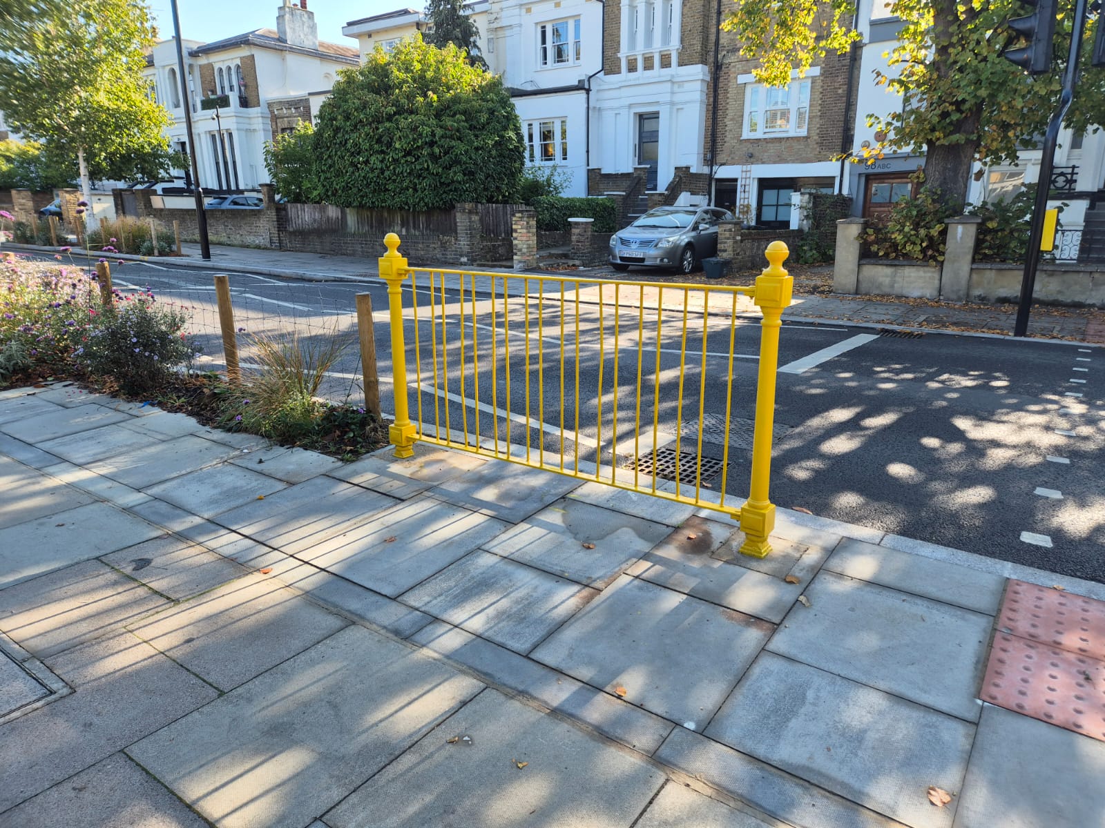 Brightly coloured metal guardrail on a pavement by the road outside a school