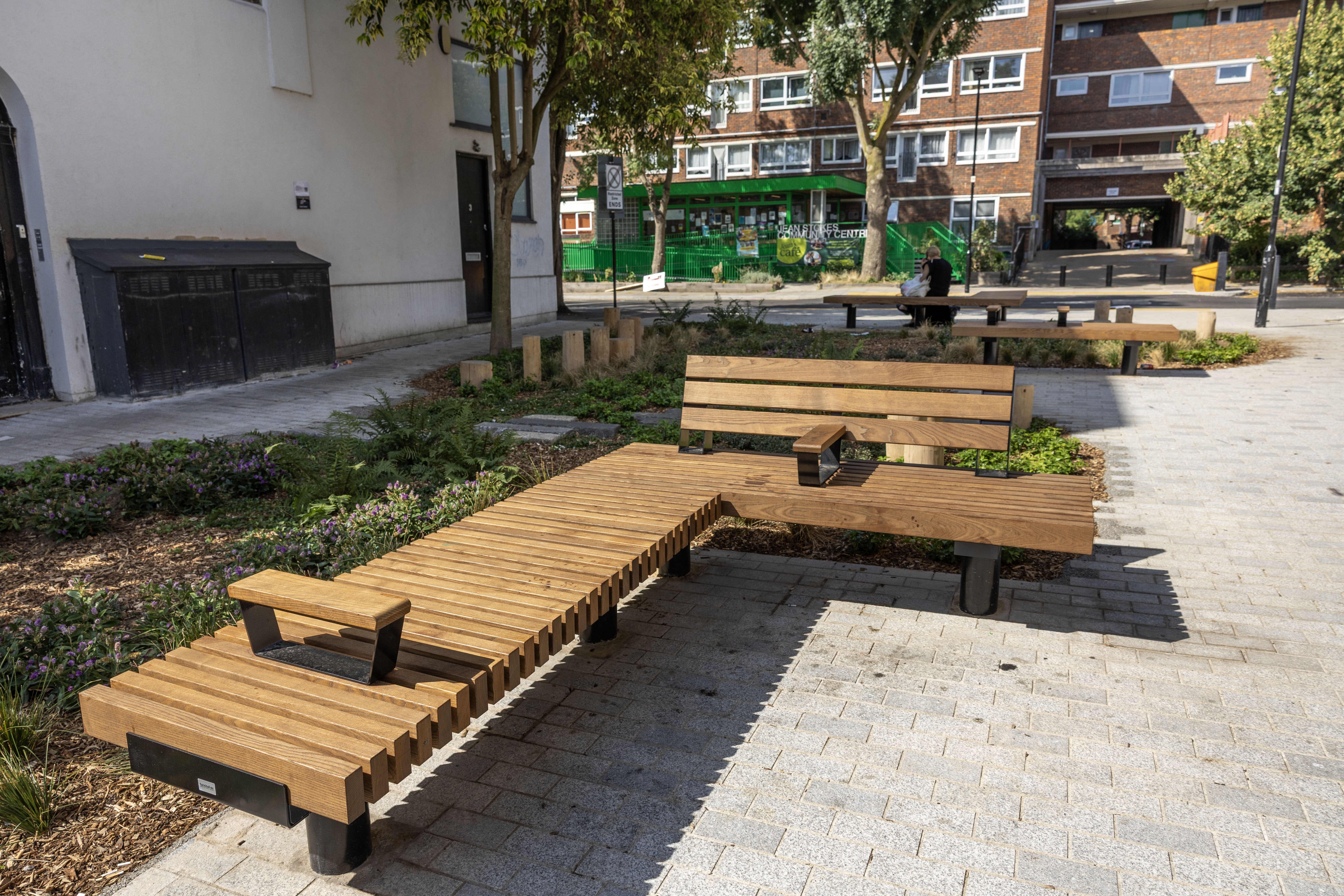 Benches on a pedestrianised paved area, with green planting alongside