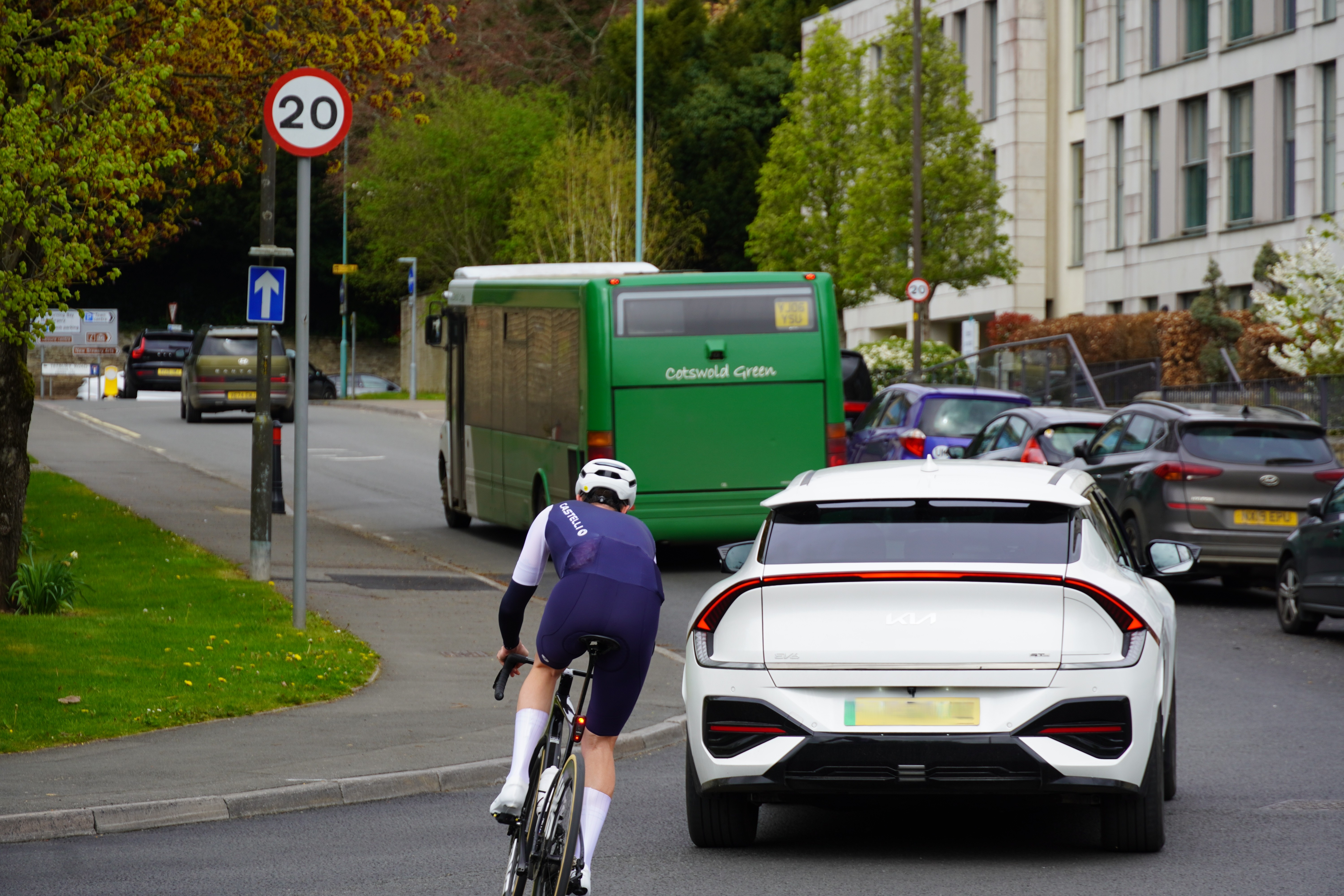  Photograph showing a section of road with a cyclist wearing a helmet, a white car, a green bus and a 20mph speed limit sign.