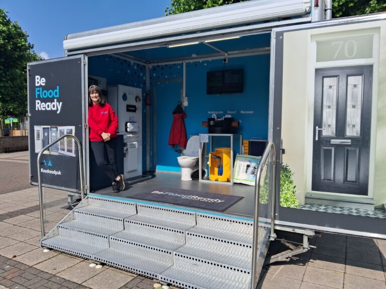 Flood Mary standing in the Flood Mobile trailer, with property flood resilience demonstration equipment on show