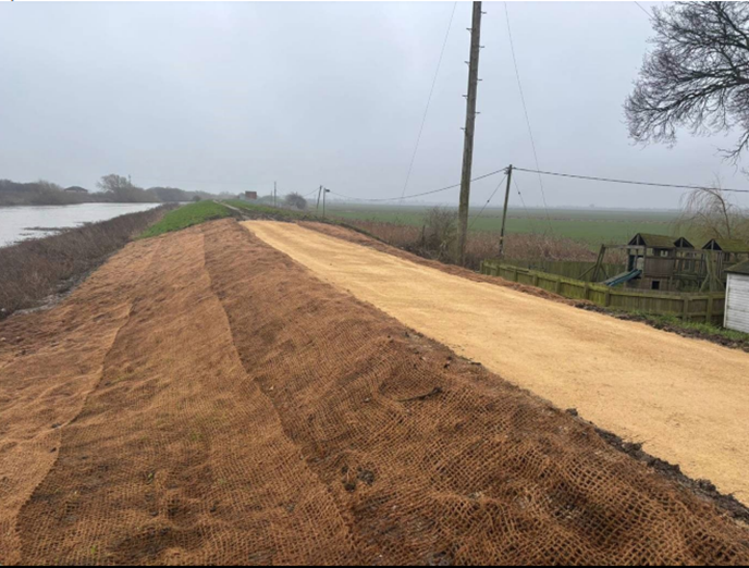 A raised river embankment with a geotextile mesh covering bare earth where a low spot has recently been repaired.