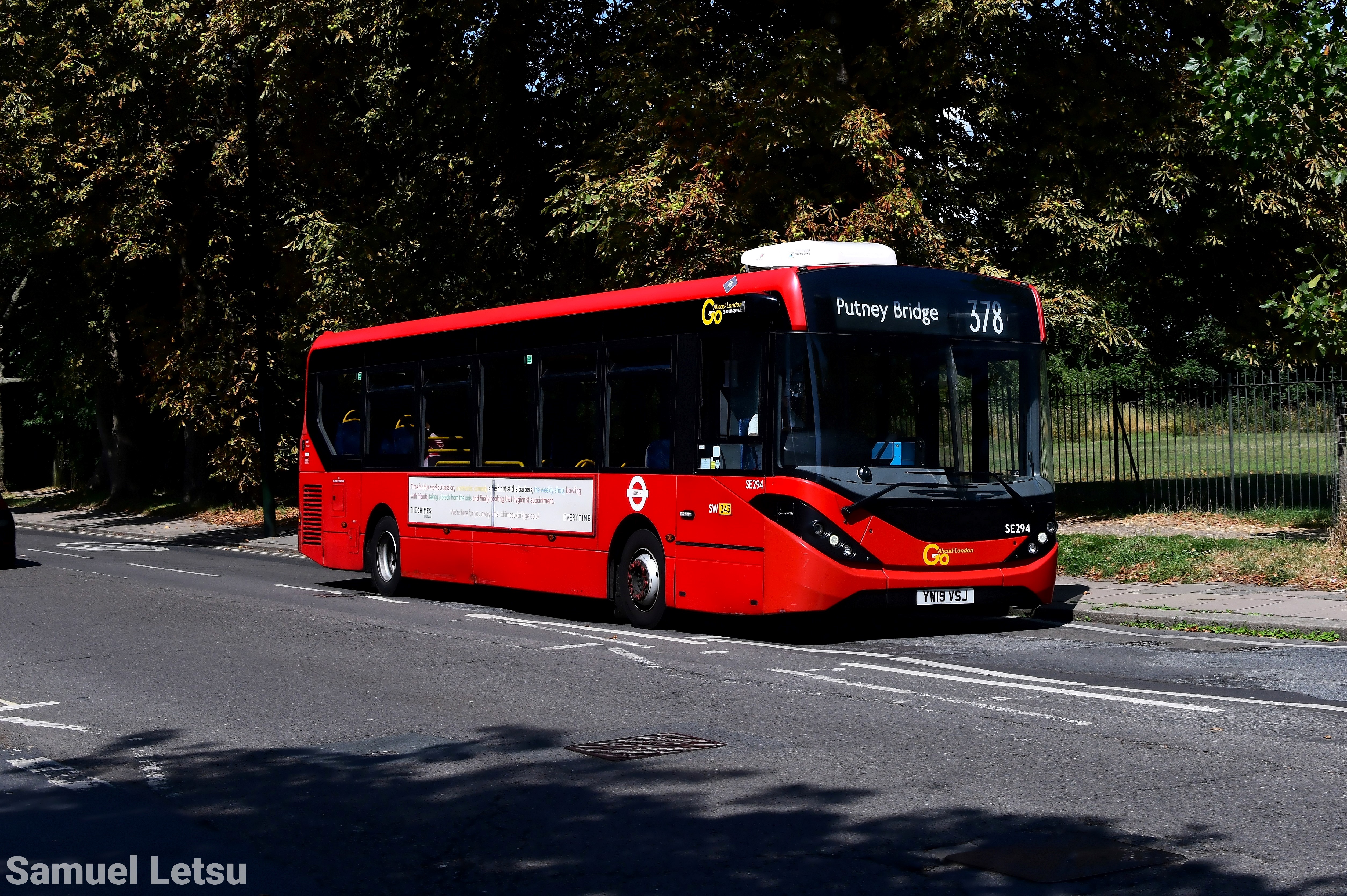 Single-decker red bus on route 378 to Putney Bridge with trees in the background