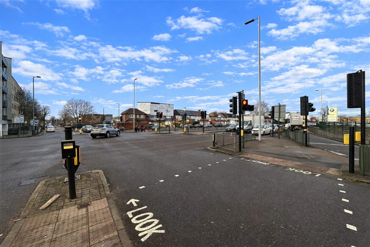 Northern ‘arm’ of the Lincoln Road junction with the A10 Great Cambridge Road with cars, traffic lights, and nearby buildings under a blue sky with scattered clouds