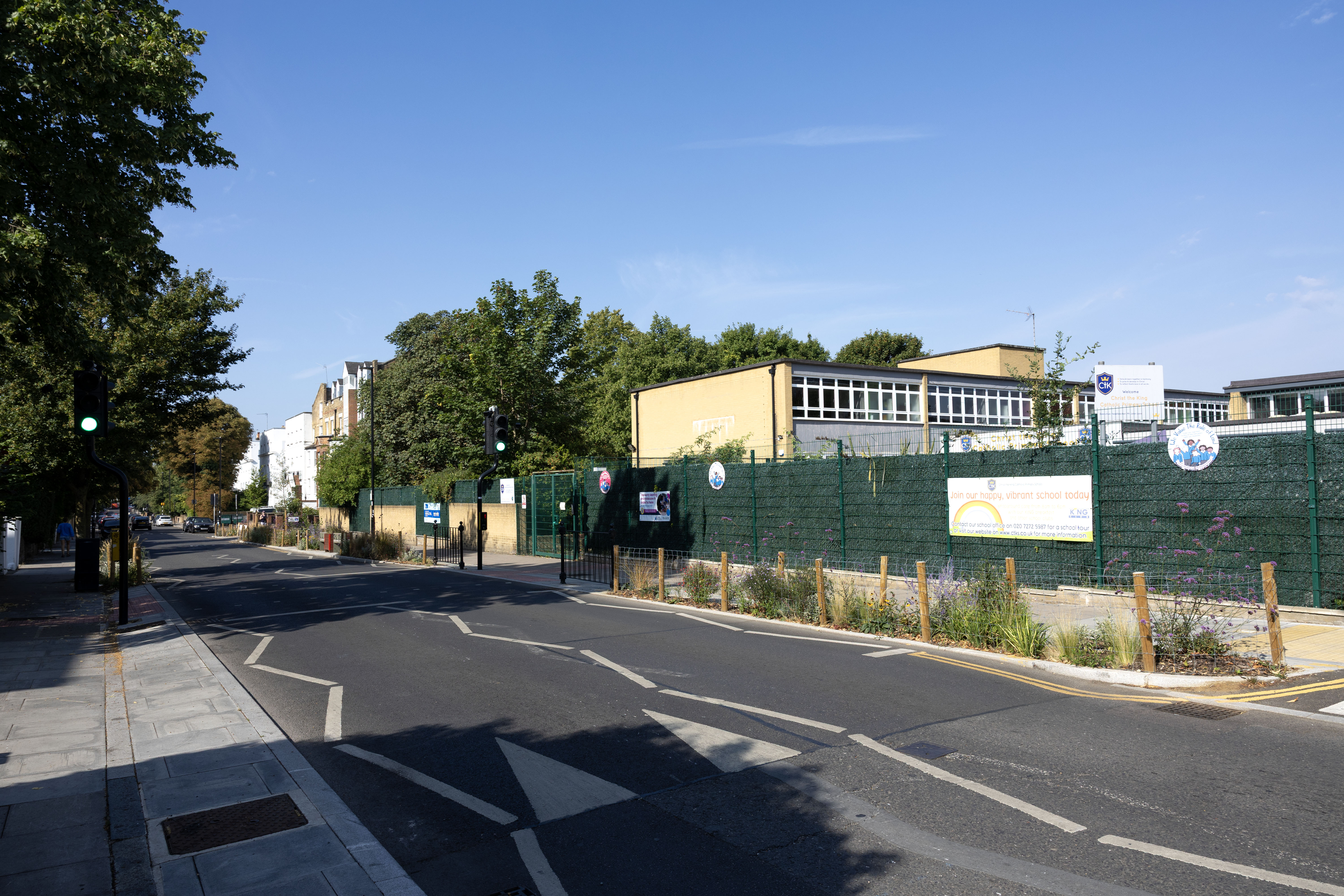 Street outside a school with planting on the pavement, and a crossing with traffic lights