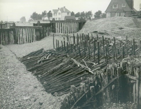 Historic photograph showing fascines used as coastal defences along a shingle beach.