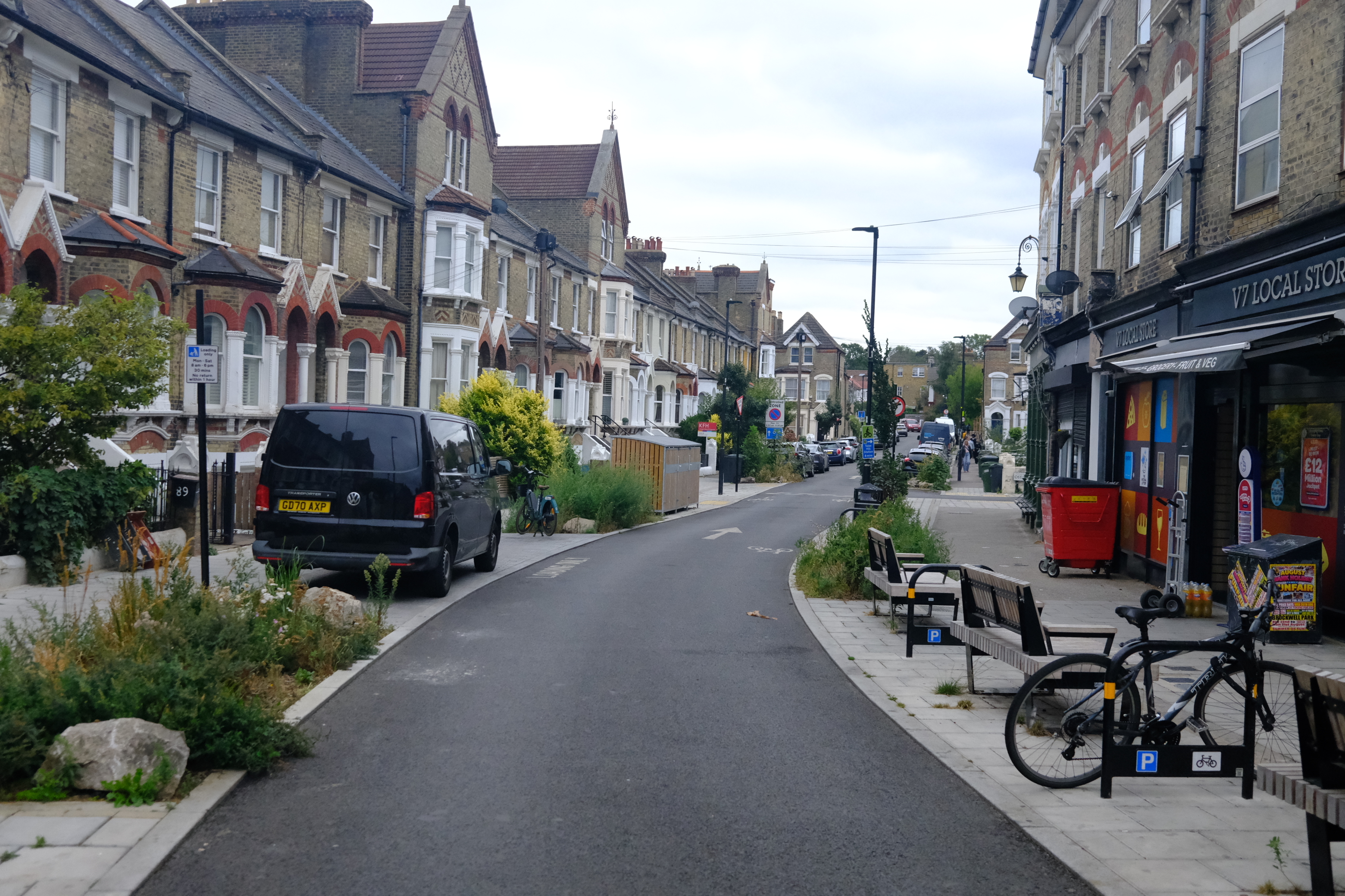 An urban street with wide pavements with benches and planting on outside shops