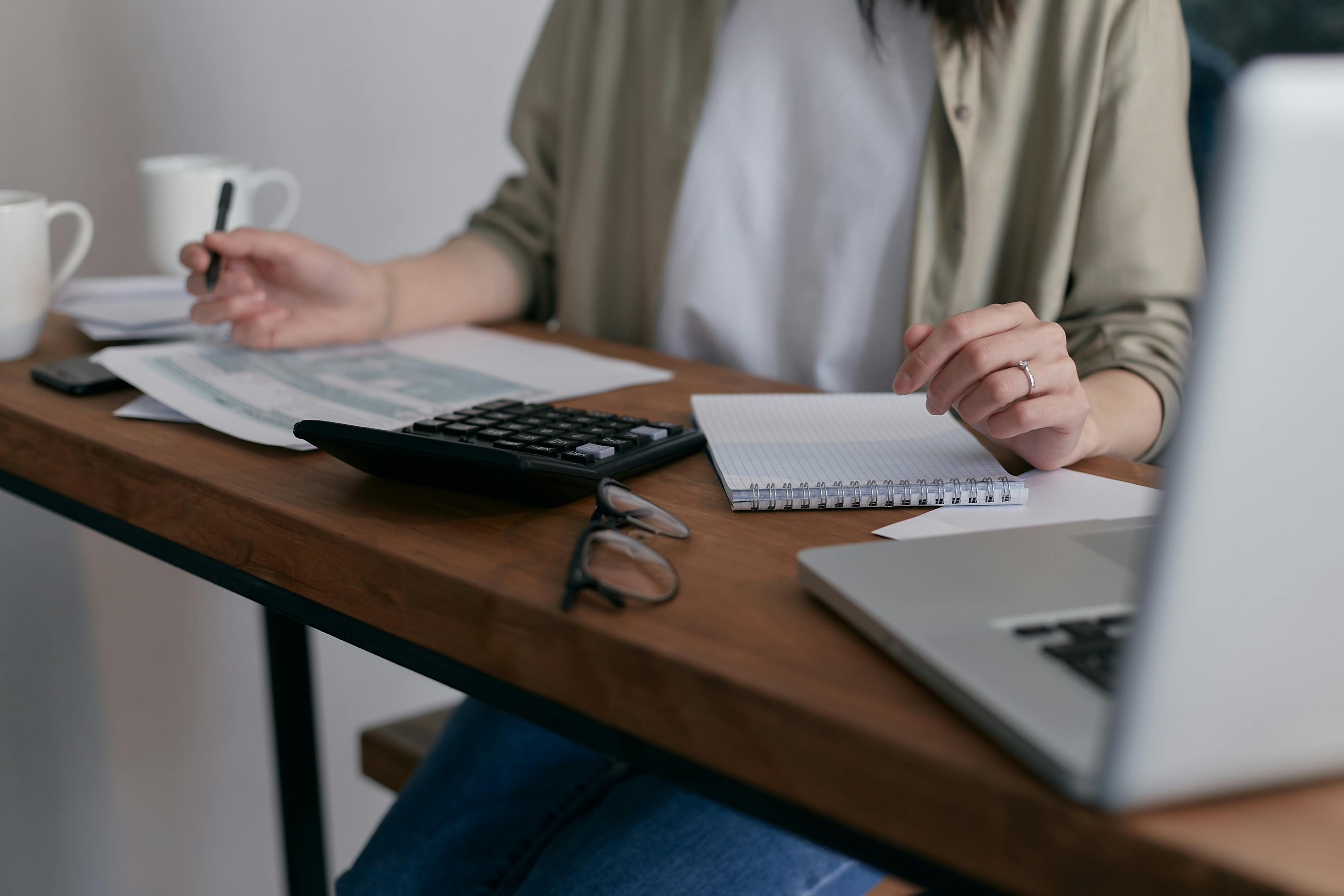 Woman sitting behind a desk with a notepad, laptop and calculator in front of her on the table.