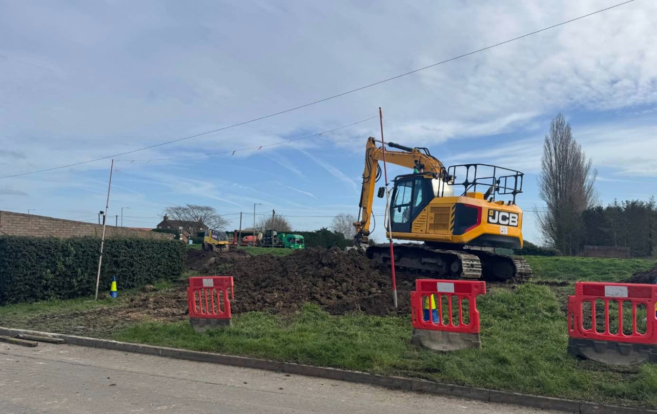 A digger moving soil on a grass verge near an embankment.