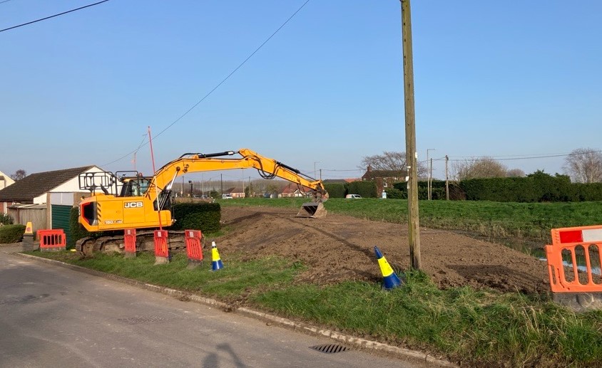 A digger using its bucket to compact soil where repairs have been made on an embankment.