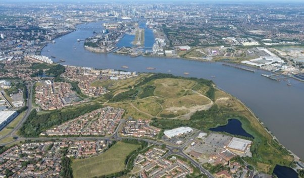 Aerial view of a riverside urban area with housing, green open land, industrial sites, and a winding river