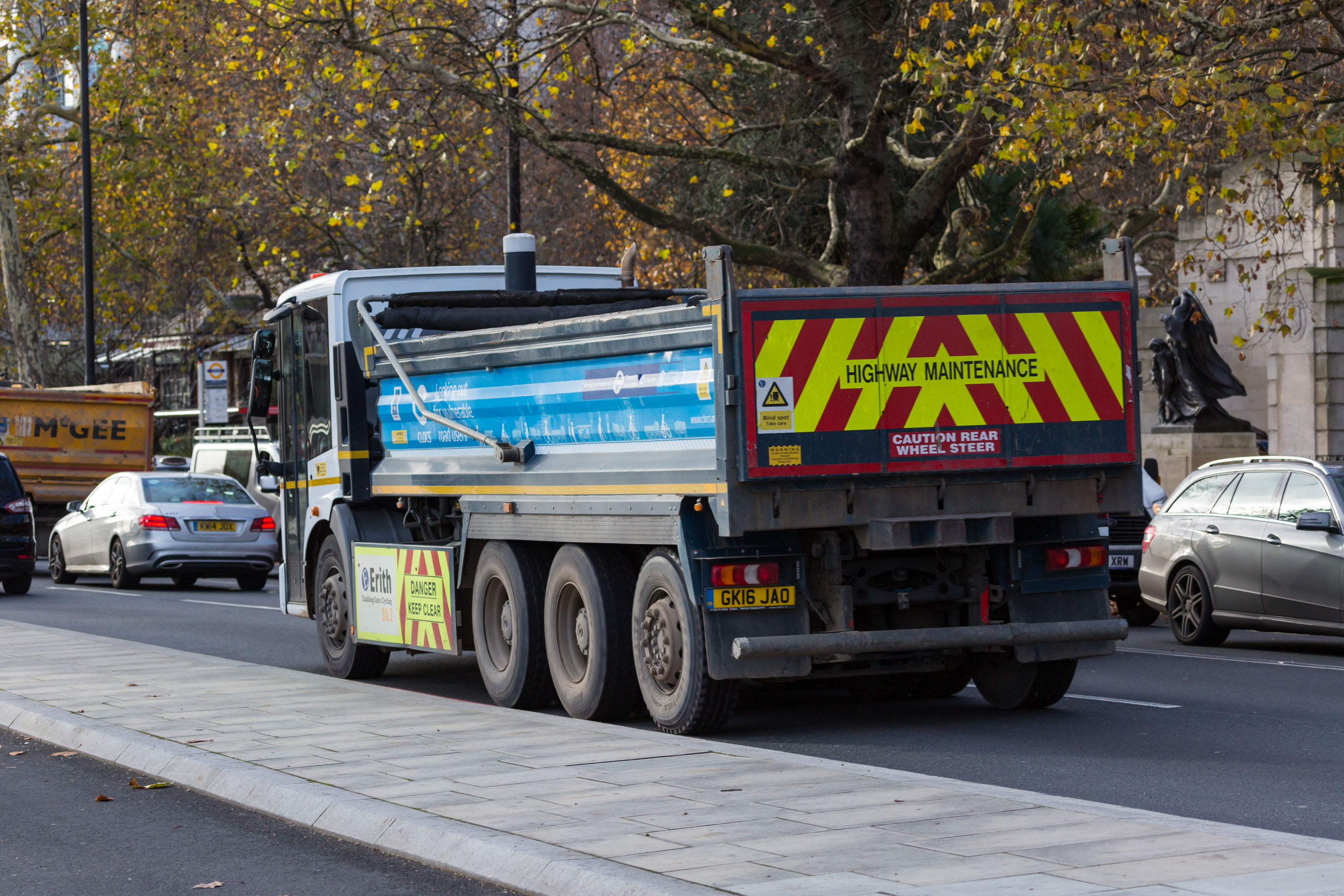Highway maintenance lorry parked on a city street with warning signage and other vehicles nearby