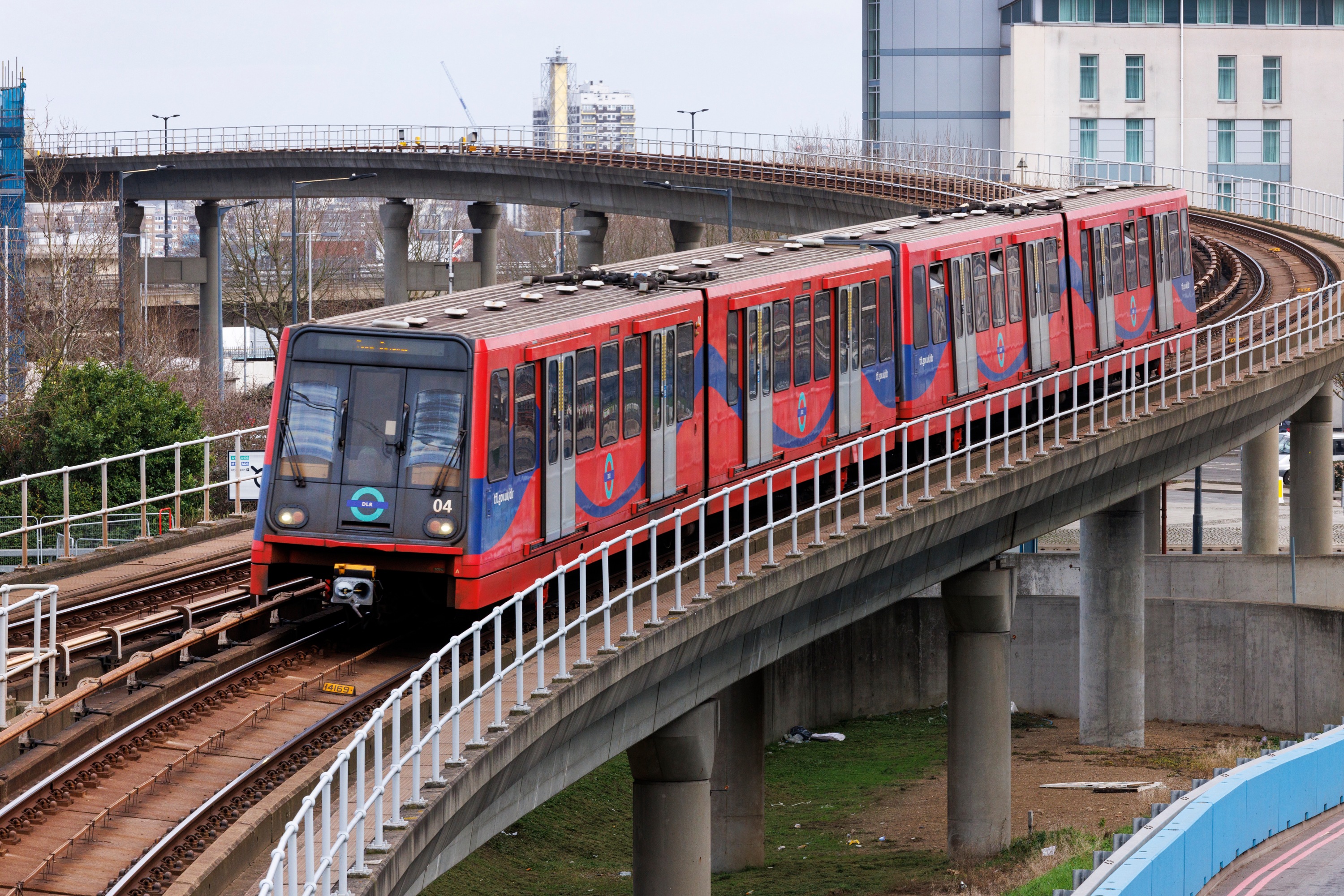 DLR train travelling on an elevated track through an urban area with buildings and overpasses in the background