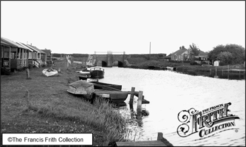 Black and White photo of Surfleet Sluice looking downstream on the River Glen, with holiday chalets and boat moorings
