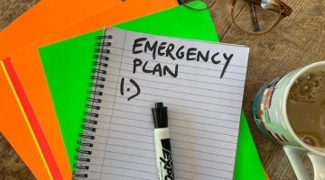 Notebook with Emergency Plan written at the top, with paper and pens and a cup of tea