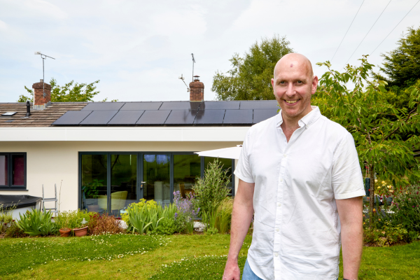 Man standing in front of bungalow with solar panels on the roof