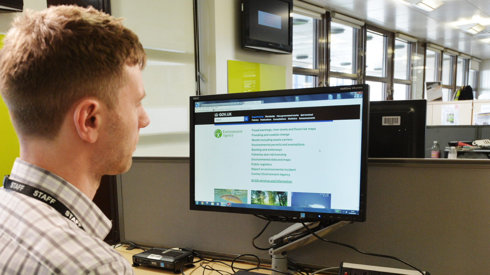 A person in an office setting sits at a desk, viewing the UK Environment Agency website on their computer monitor.