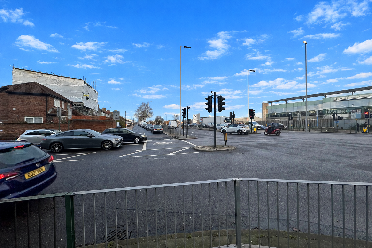 A10 junction with Lincoln Road showing multiple cars, traffic lights, and residential buildings, viewed under a bright blue sky with scattered clouds