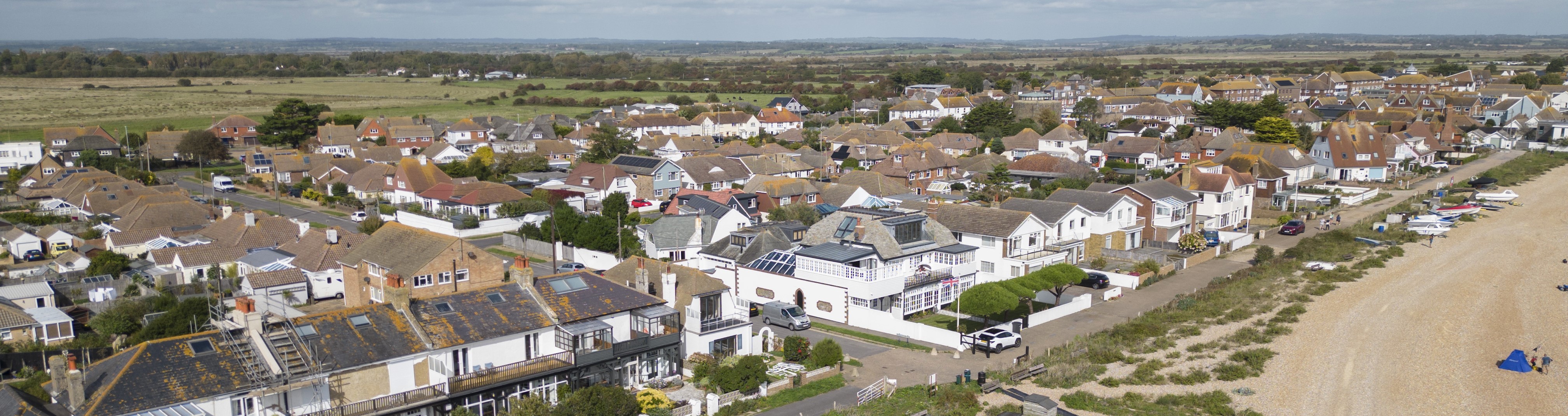 Aerial view of Pevensey Bay showing houses along the coastline with the beach and open countryside in the background.