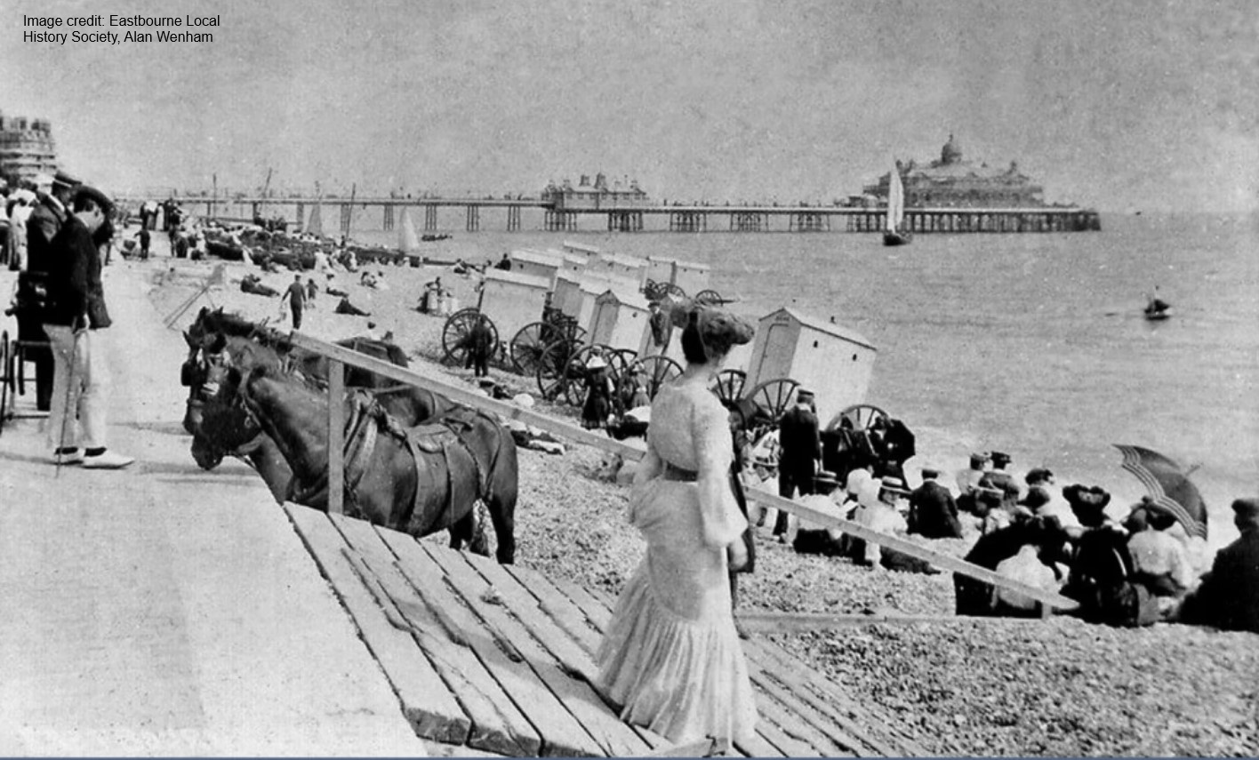 Historical image of Eastbourne beach and pier with bathing machines and horses.