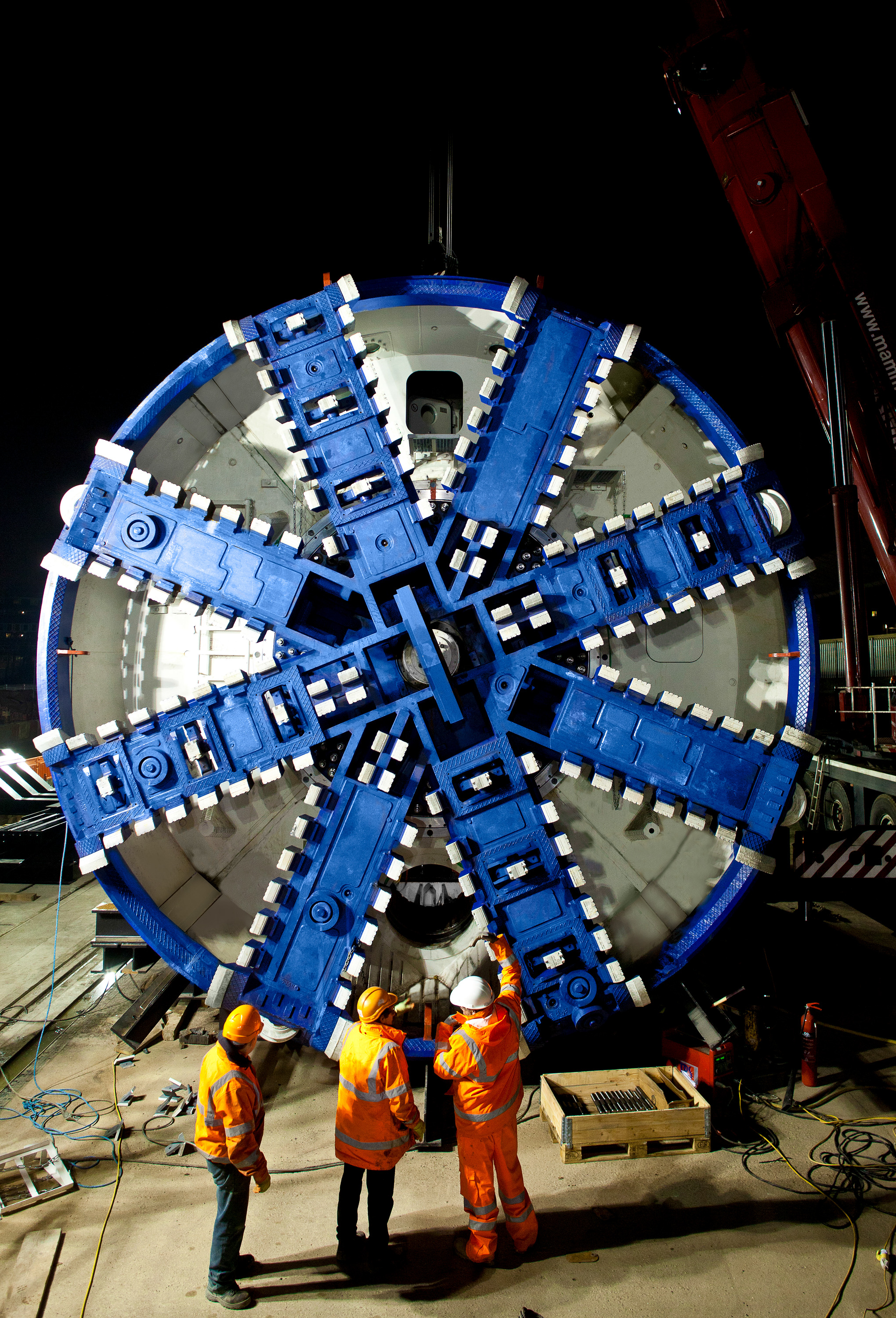 Large tunnel boring machine cutter head being inspected by workers in high-visibility clothing at a construction site