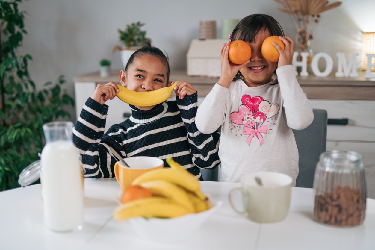 Two children holding up fruit in front of their faces