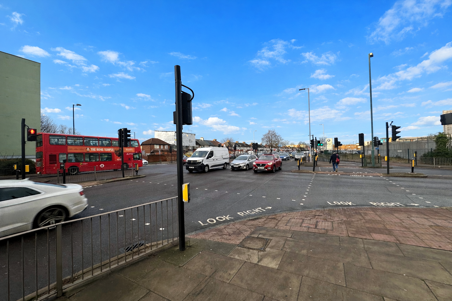 A10 Great Cambridge Road junction with Lincoln Road showing the existing pedestrian crossings with cars, a red bus, and pedestrians at traffic lights under a bright blue sky