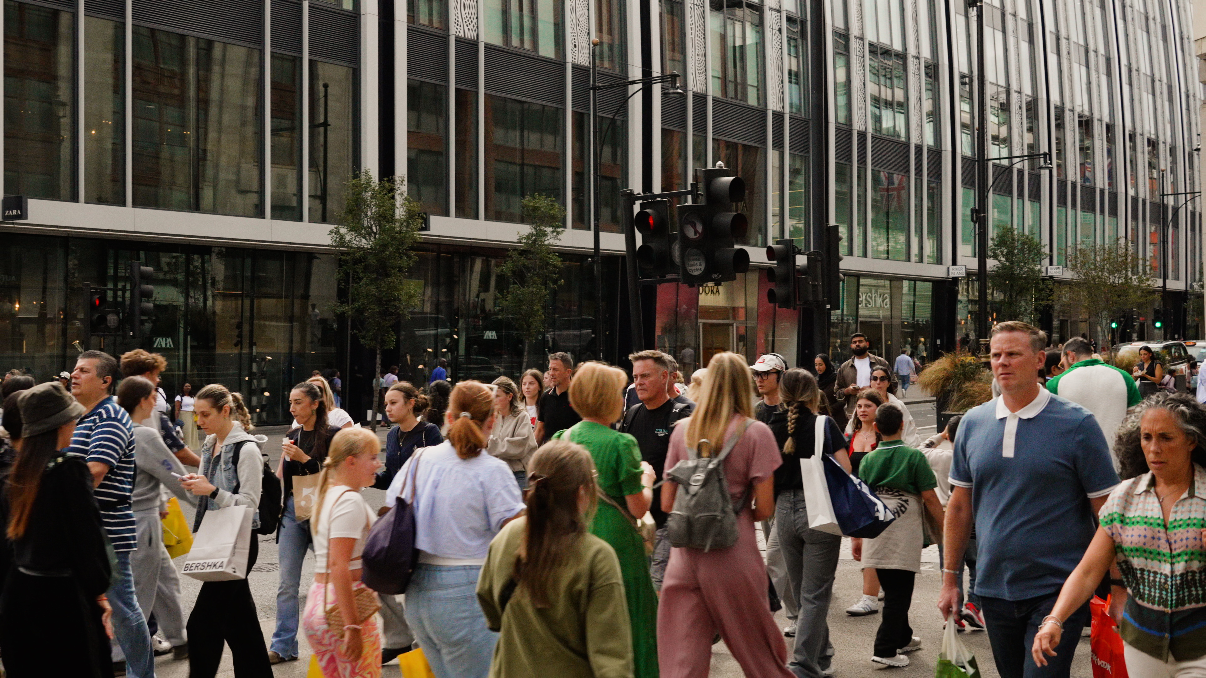 Busy Oxford Street scene with pedestrians walking past shops and a modern glass-fronted building in the background