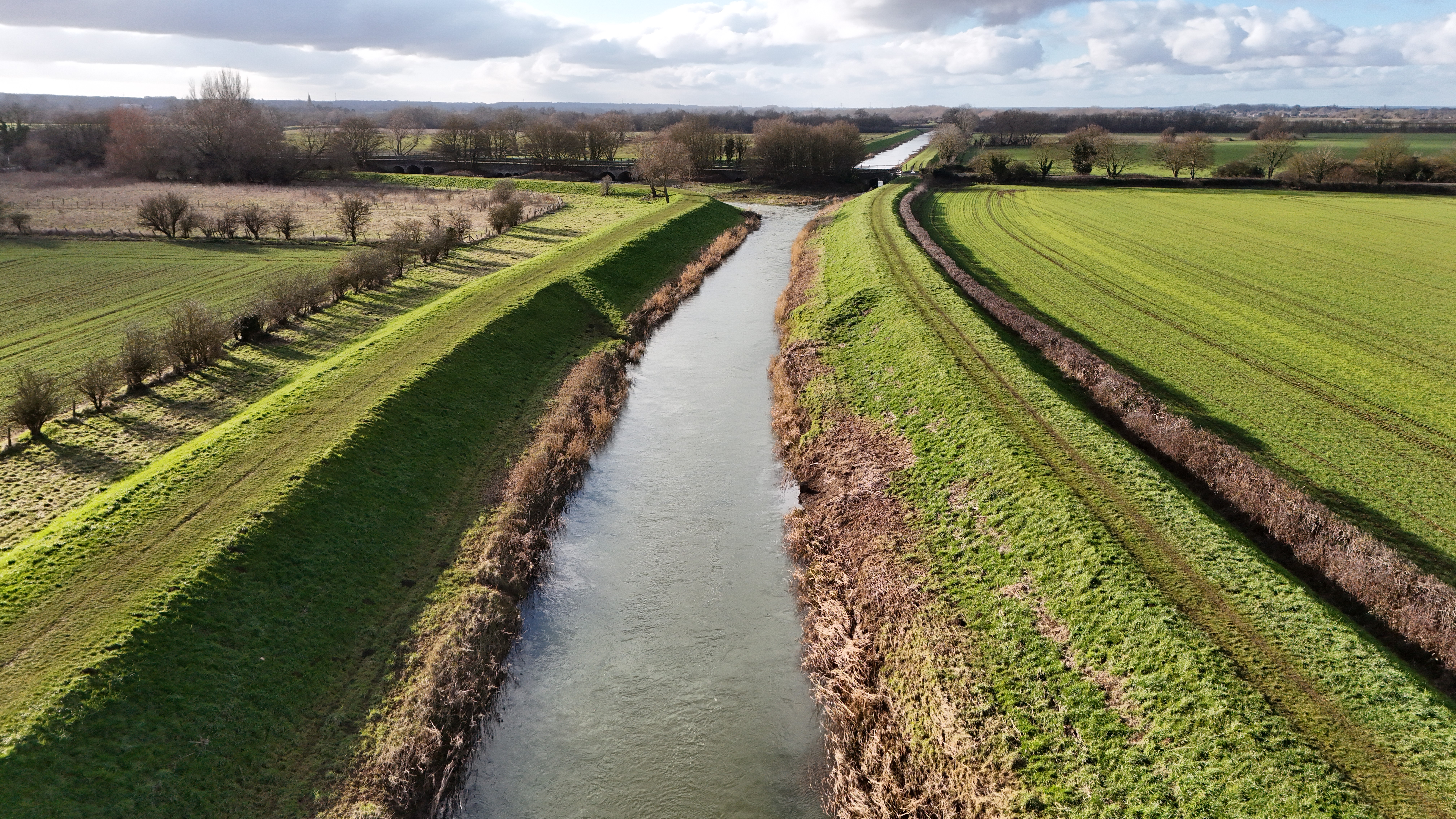 Photograph taken from a drone showing an aerial view from medium distance of the Maxey Cut river channel with raised earth embankments on either side of the river.
