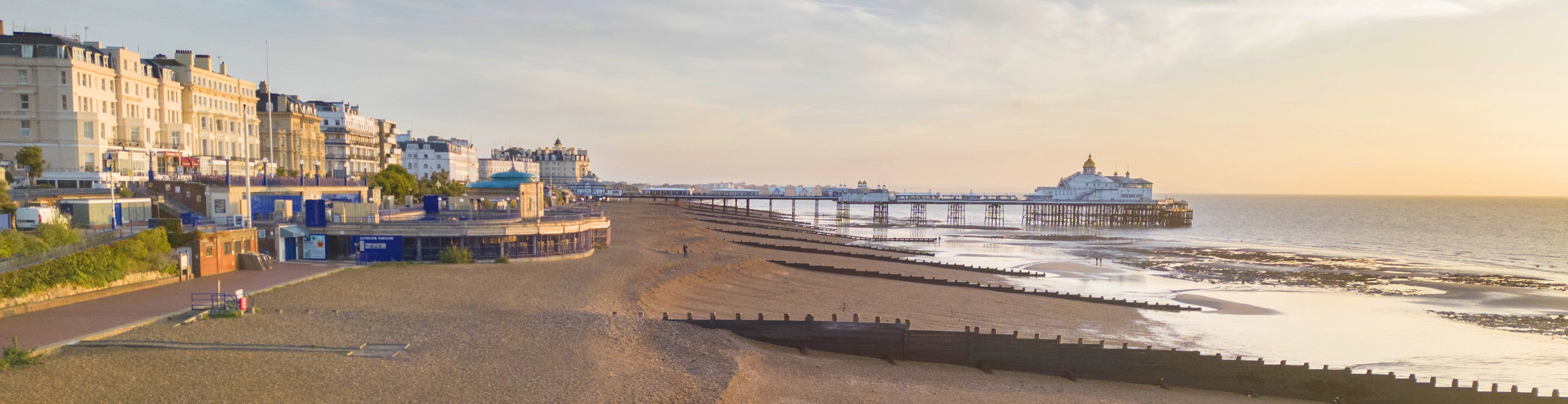 View of Eastbourne beach at low tide, with the pier extending over the sea and seafront buildings lining the promenade.