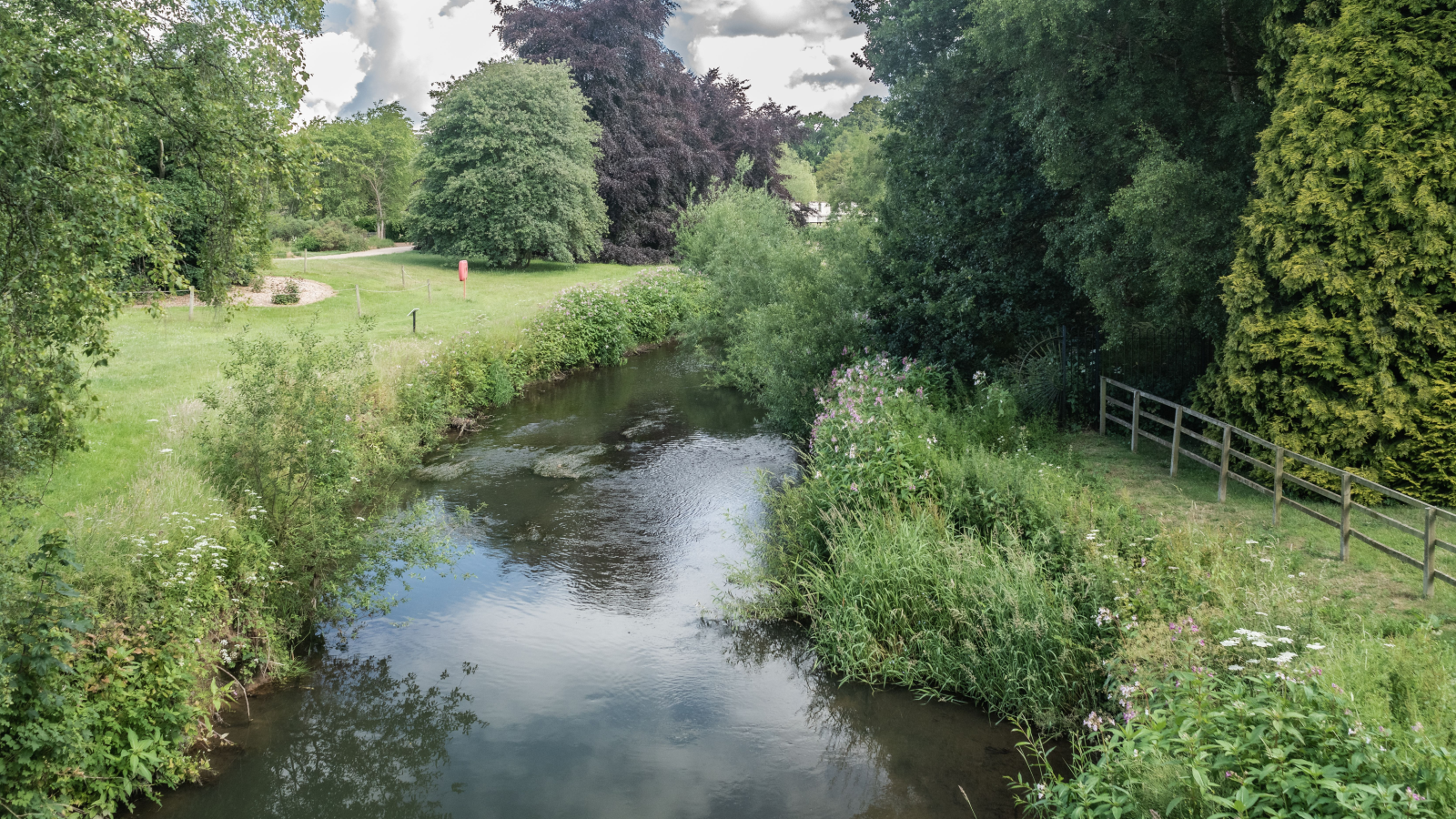 A serene landscape featuring a gently flowing stream surrounded by lush greenery and trees under a partly cloudy sky.