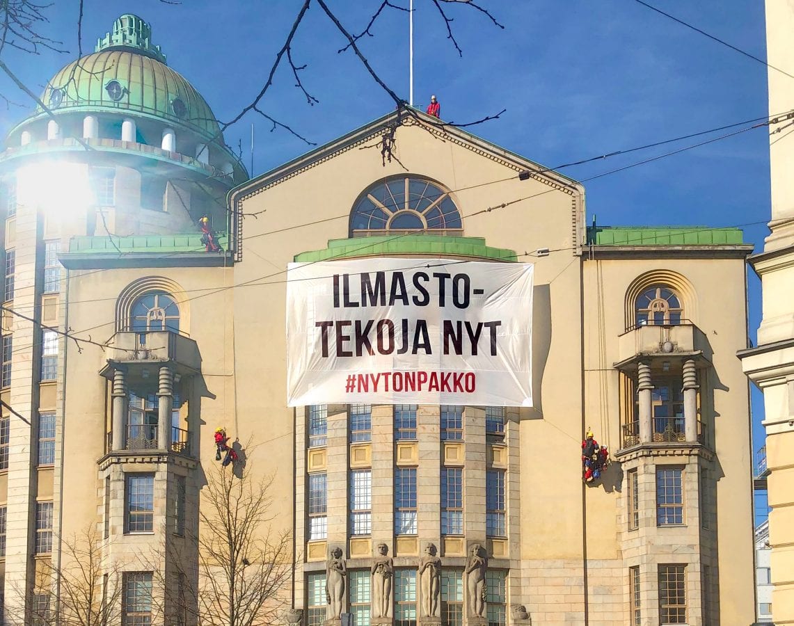 Greenpeacen kiipeilijät ripustavat aurinkoisena päivänä Uuden ylioppilastalon seinään banderollia, josta lukee isoilla mustilla kirjaimilla 'Ilmastotekoja nyt!'