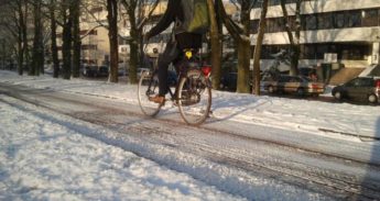 Fietser glibbert over fietspad met sneeuw en ijs