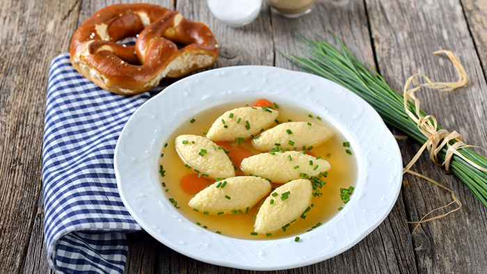  Ein Teller Grießnockerlsuppe mit einer Breze, einem Bund Schnittlauch und einer Serviette / mauritius images / Karl Allgäuer