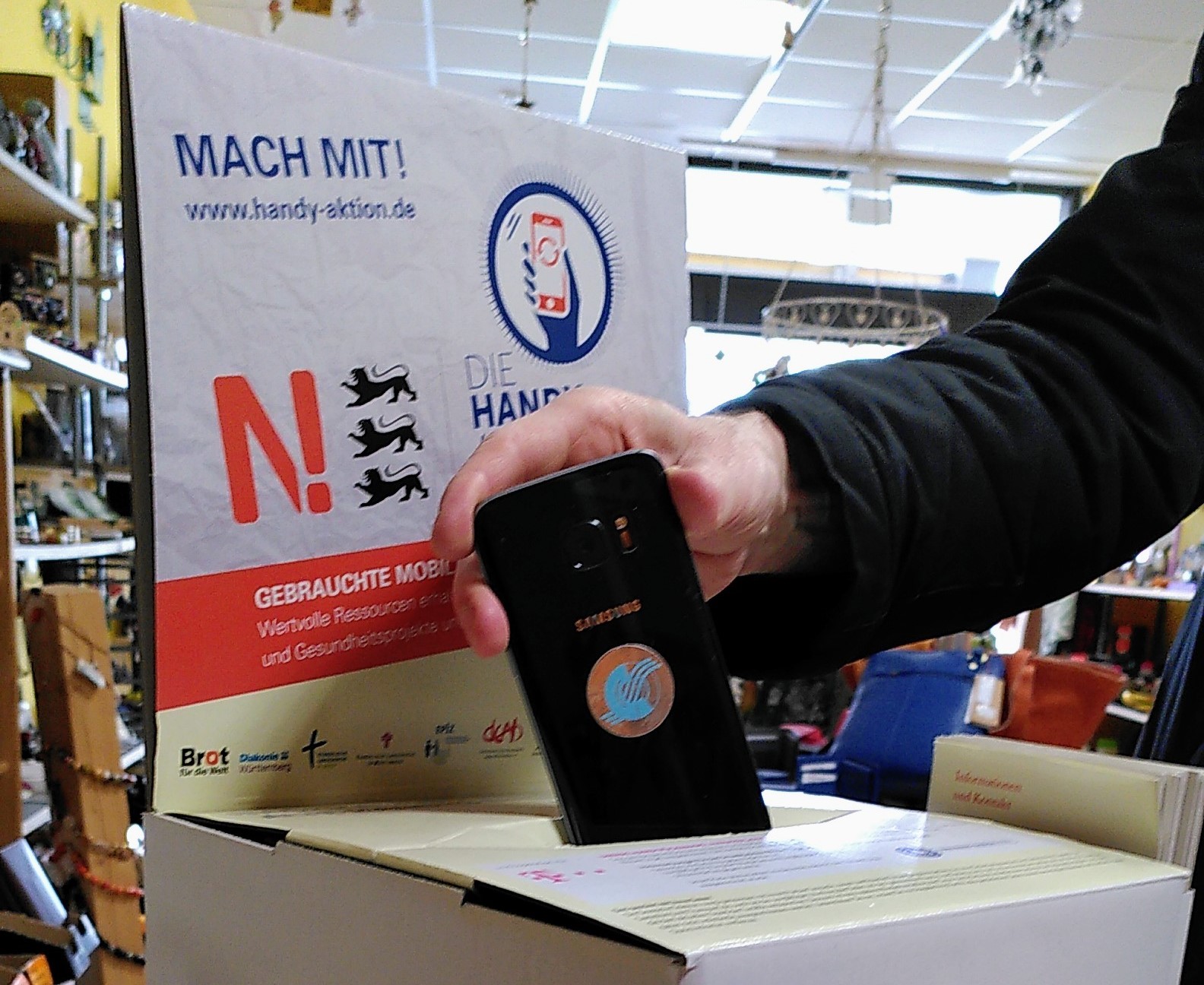 Jemand steckt ein altes Handy in eine Sammelbox.