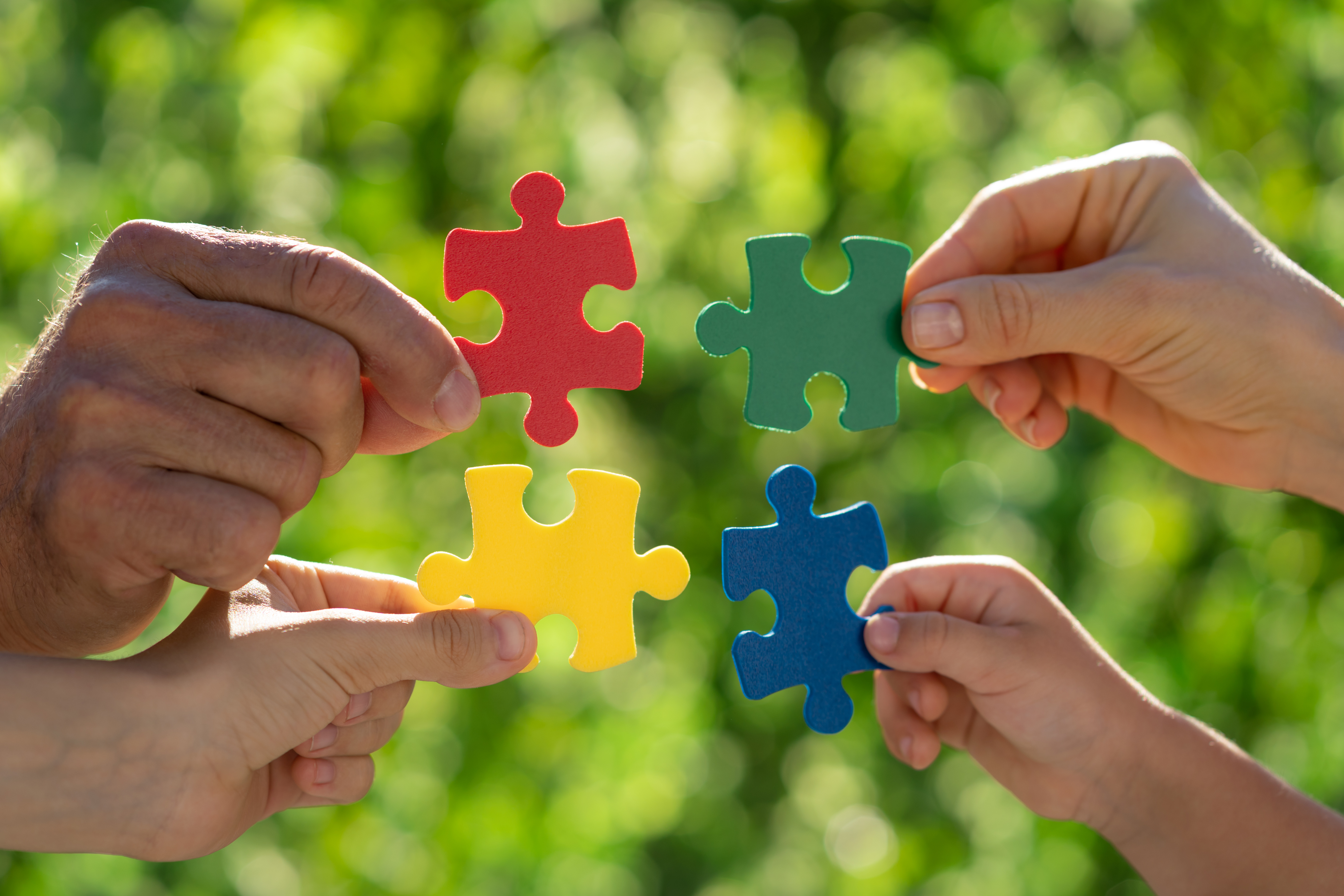 Vier Hände mit unterschiedlichen Hautfarben halten vier Puzzleteile.